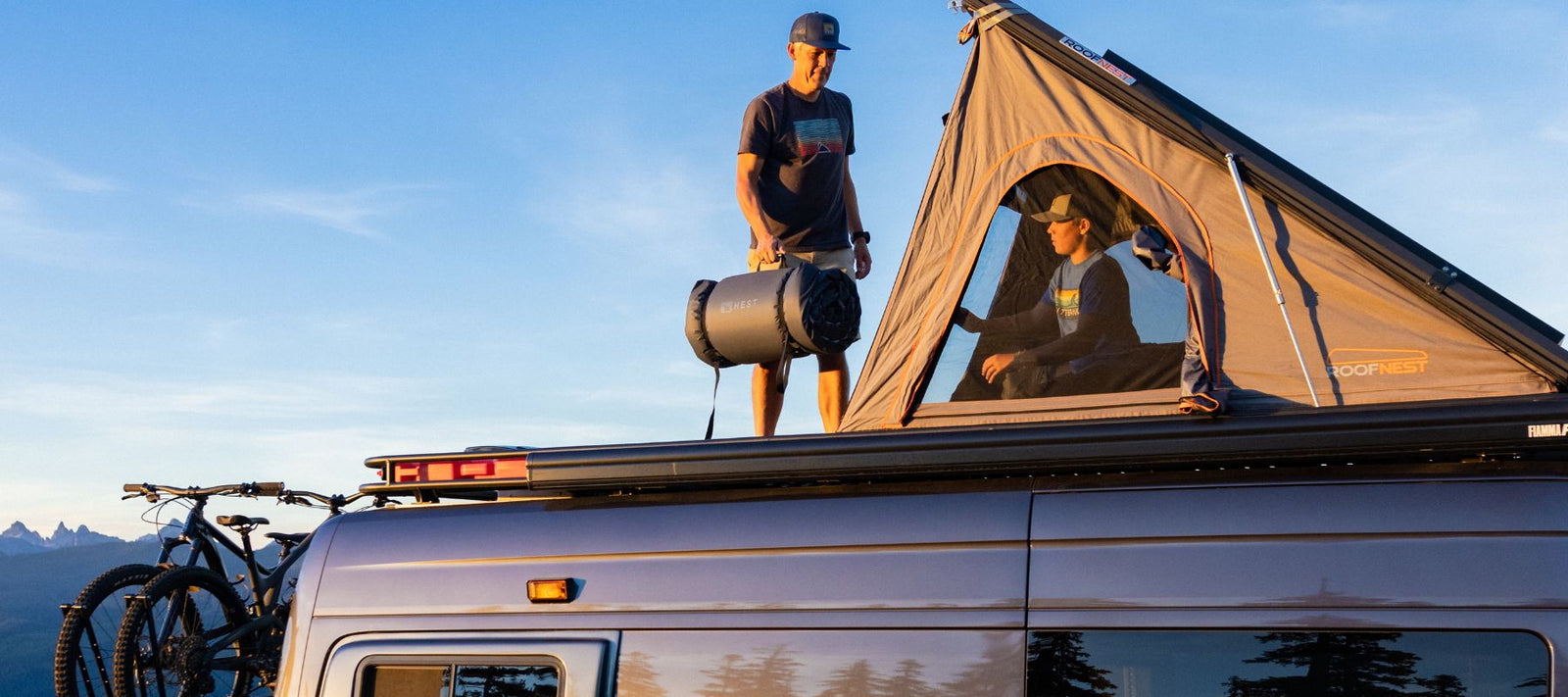 two people standing on top of sprinter van with rooftop tent